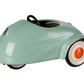 A glossy mint green vintage-style pedal toy car with a black steering wheel, black tires, and white-walled wheels with orange center caps, shown on a plain white background.