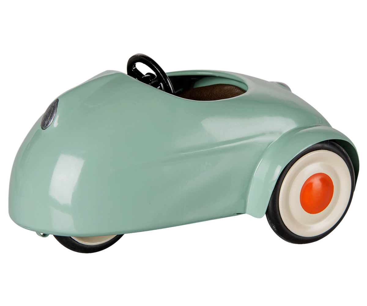 A glossy mint green vintage-style pedal toy car with a black steering wheel, black tires, and white-walled wheels with orange center caps, shown on a plain white background.