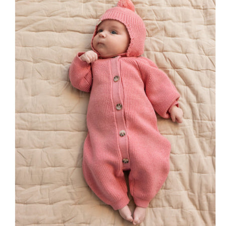 Baby in a pink outfit lying on a beige quilted surface