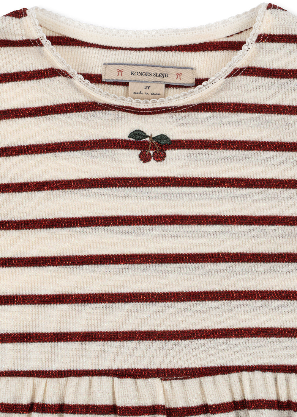 Close-up of a striped knit top with horizontal burgundy and cream stripes, a small embroidered cherry motif at the center chest, and a visible neck label reading KONGES SLAVID.