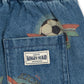 Close-up of blue denim shorts with an elastic waistband, a back pocket, and soccer ball prints. A white brand label reading 'KONGES SLOJ' is sewn into the pocket.