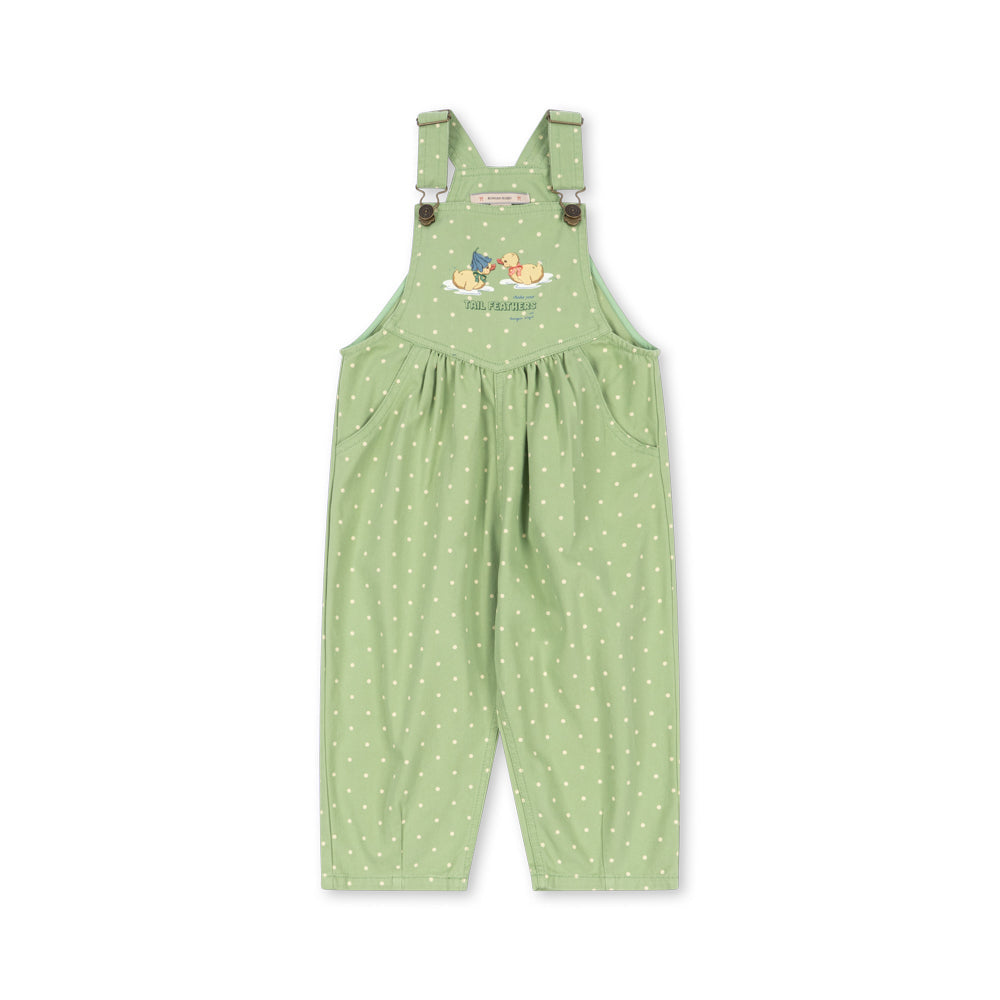 A light green children's overall jumpsuit with white polka dots, featuring adjustable shoulder straps with small brown buttons and a colorful cartoon graphic on the chest, displayed against a solid white background.