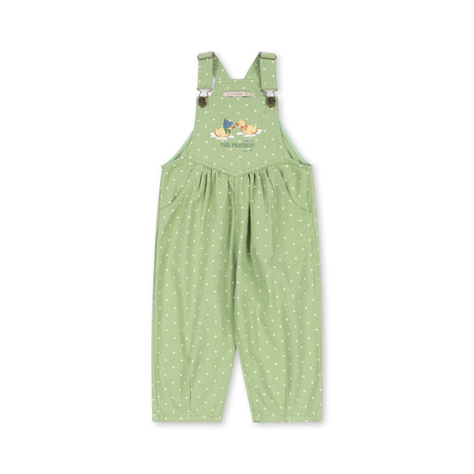 A light green children's overall jumpsuit with white polka dots, featuring adjustable shoulder straps with small brown buttons and a colorful cartoon graphic on the chest, displayed against a solid white background.