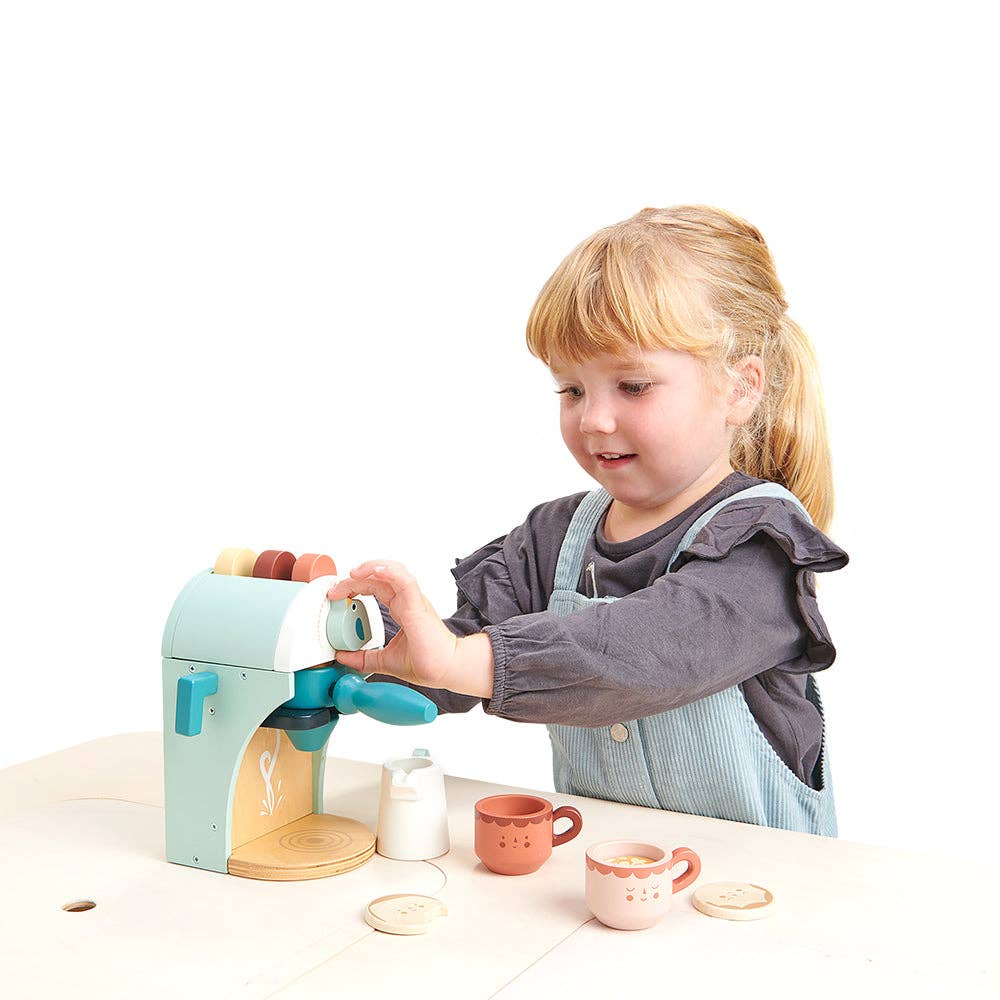 Child playing with a toy coffee machine and cups on a white background