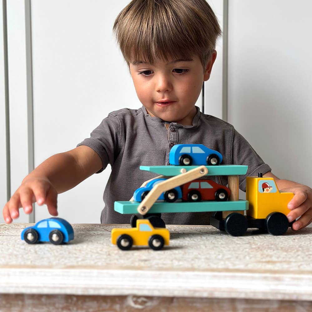 Child playing with a toy car carrier and cars on a wooden surface.