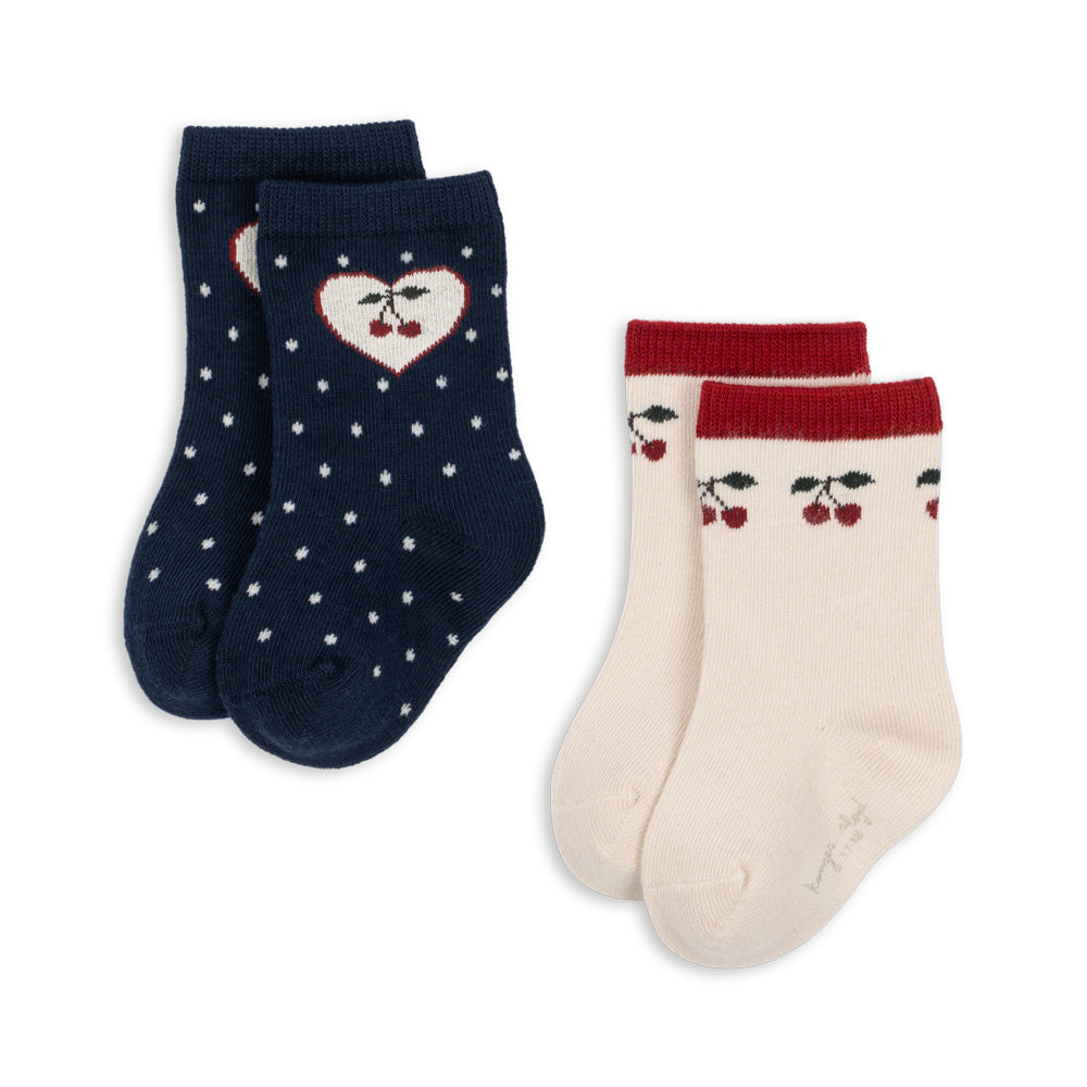A 2-pack of children's crew socks on a white background. One pair is navy blue with white polka dots and a heart motif containing cherries.