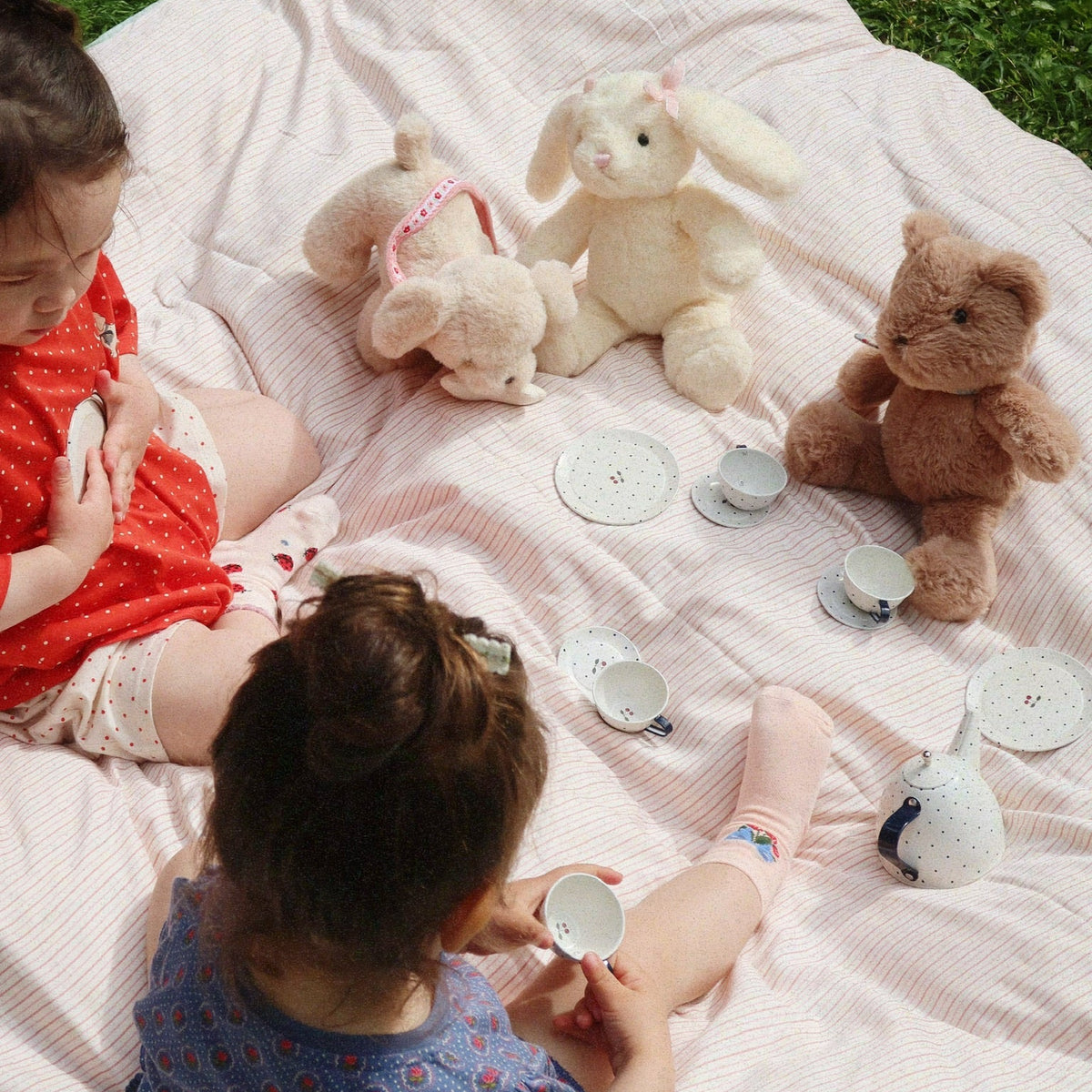 Two children playing with toys on a blanket outdoors.