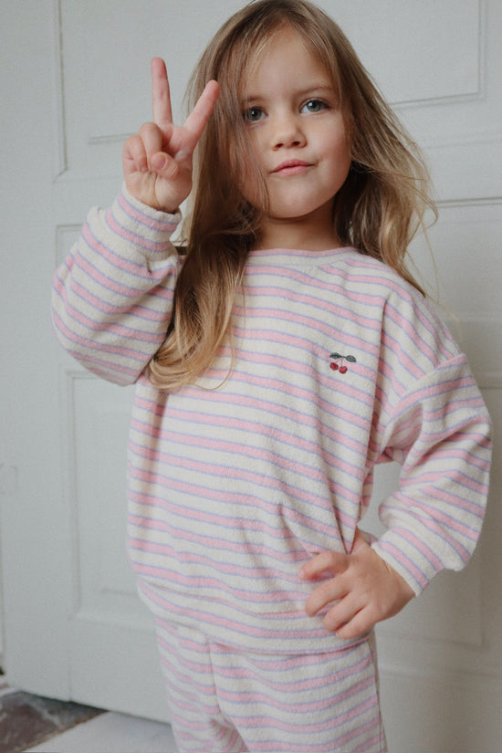 Child wearing a pink and white striped outfit with a cherry design, making a peace sign.