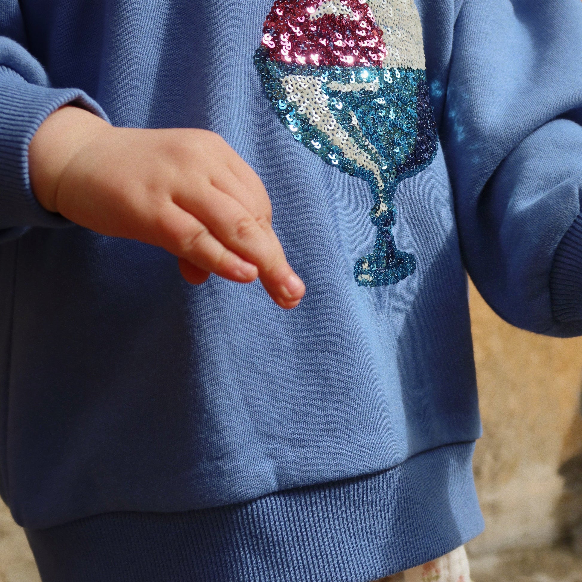 Blue sweatshirt with ice cream cone design worn by a child, blurred background