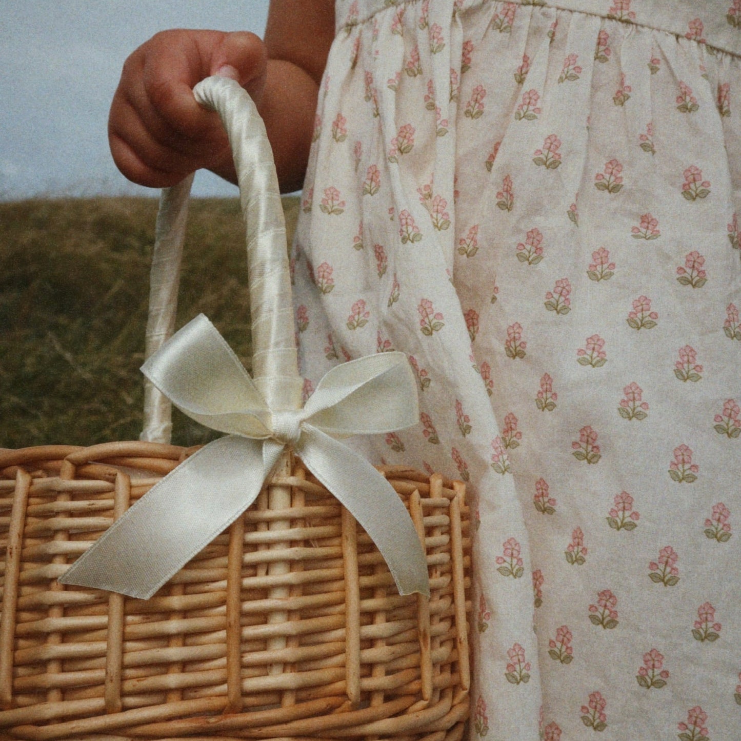 Person wearing a floral dress holding a wicker basket with a bow.