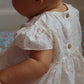 Baby wearing a white dress with small red patterns