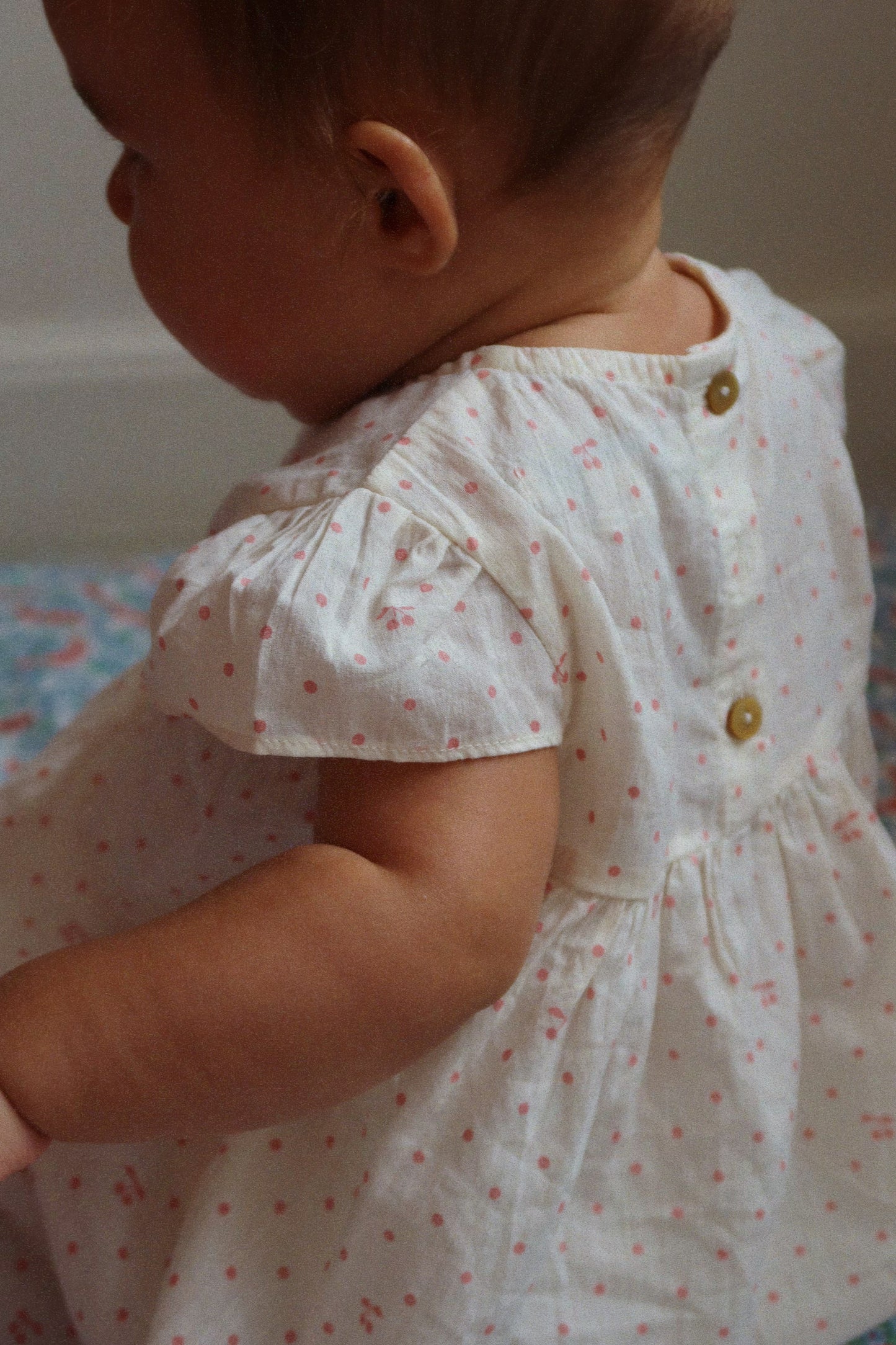 Baby wearing a white dress with small red patterns