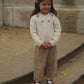 Young girl in a cream sweater and checkered pants standing on steps with a stone wall background
