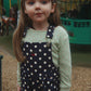 Young girl in a polka dot dress standing in front of a carousel.