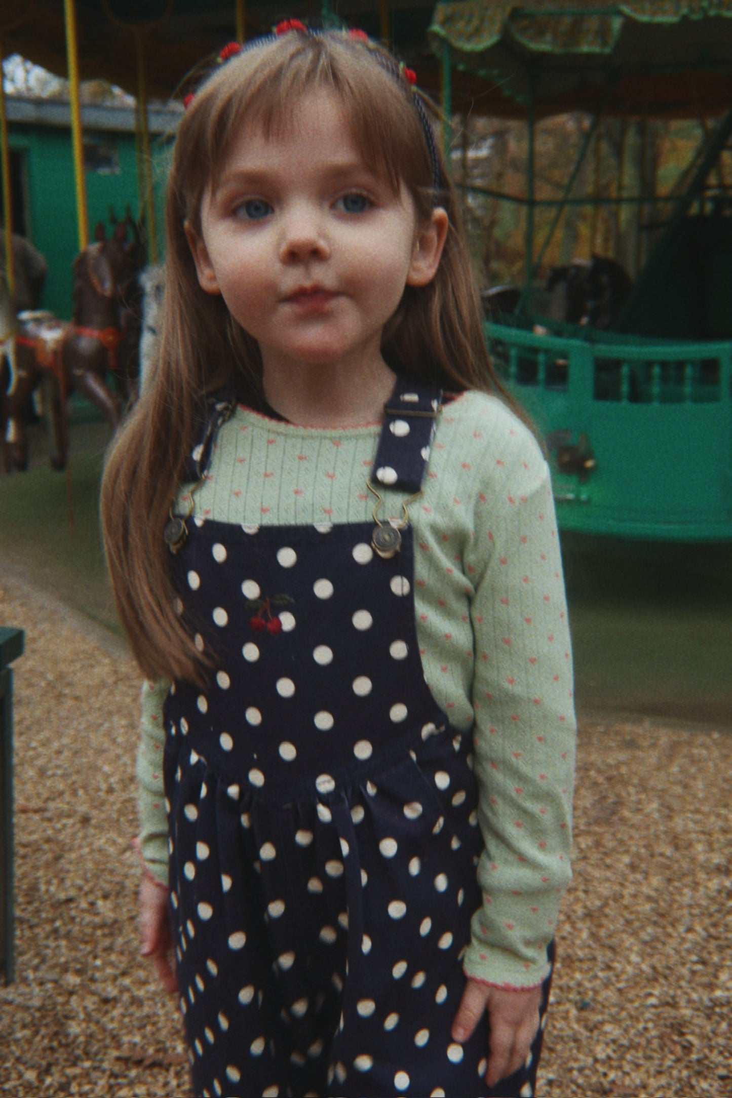Young girl in a polka dot dress standing in front of a carousel.