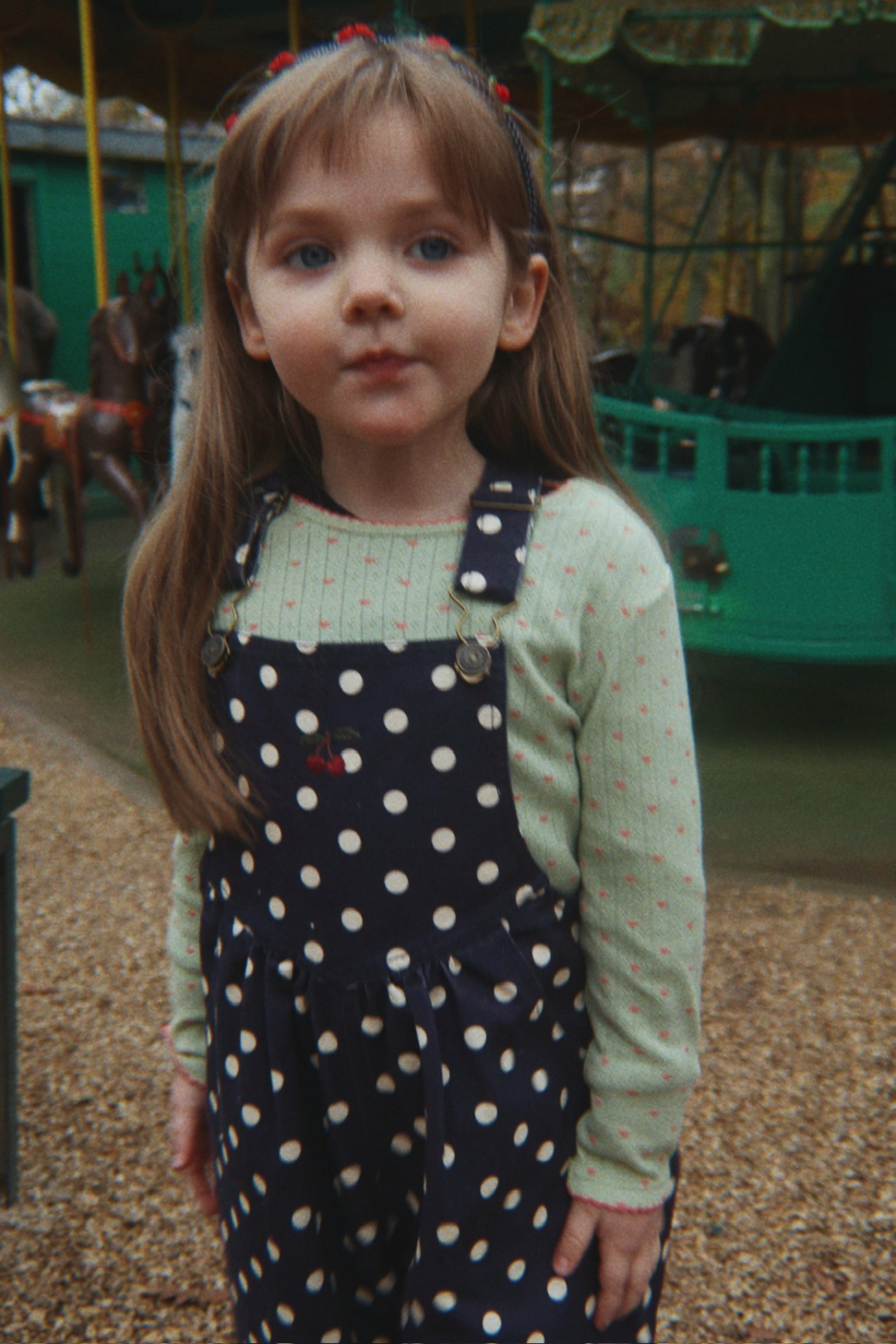 Young girl in a polka dot dress standing in front of a carousel.