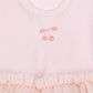 Close-up of a light pink children's dress with a glittery pink cherry motif on the chest and a ruffled tulle skirt with tiny gold speckles.