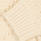 Close-up of a cream-colored knit sweater showing a ribbed cuff and textured openwork knit pattern.