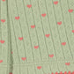 Close-up of a light sage green knit fabric with a repeating pattern of small pink hearts and a pink scalloped edge.