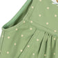 Close-up of a light green children's dress with white polka dots, showing the shoulder strap, neckline, and pleated skirt detail.