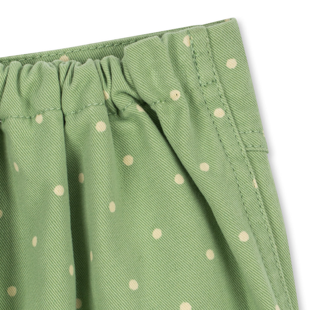 Close-up of a green fabric garment with a white polka dot pattern and an elastic waistband, shown against a plain white background.