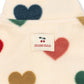 Close-up of a cream-colored fuzzy garment with large heart shapes in navy, red, green, brown, and tan, featuring a sewn-on brand label that reads 'KONNES CLOJ' with a cherry graphic.